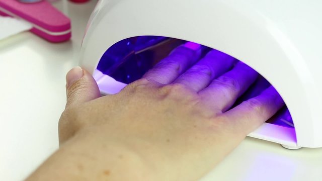 Manicure in process - putting hand and curing gel varnish in nail LED lamp, procedure of polymerization