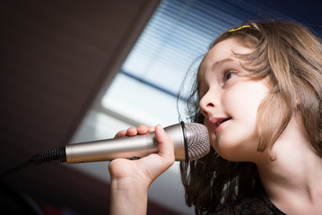 Little cute girl singing karaoke on microphone at home