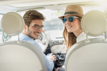 rear view, cheerful couple inside car, looking at camera