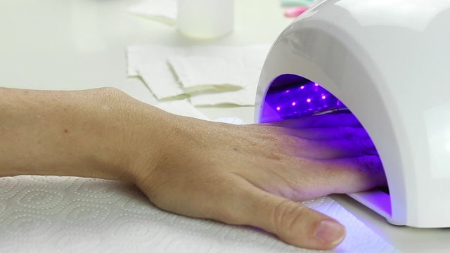 Manicure in process - putting hand and curing gel varnish in nail LED lamp, procedure of polymerization