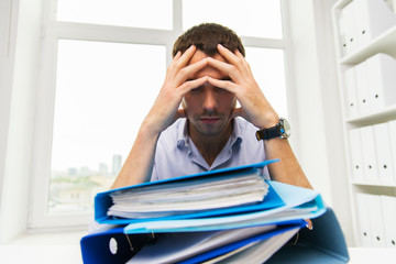sad businessman with stack of folders at office