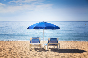 Two sun beds with blue umbrella on a tropical beach with a beautiful ocean view
