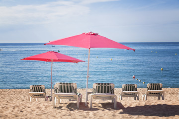 Four sun beds with two pink umbrellas on a tropical beach with a beautiful ocean view