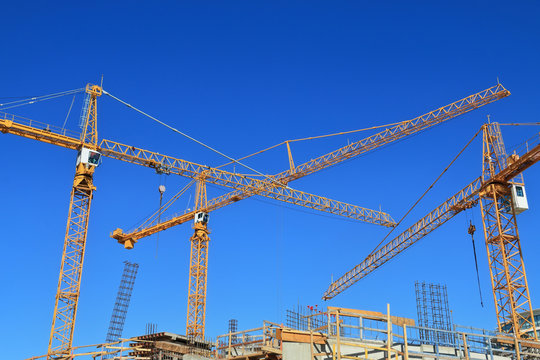 Three construction cranes and building against blue sky.