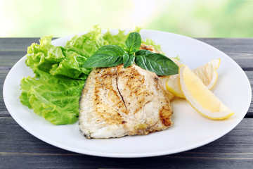 Dish of fish fillet with greens and lemon on table close up