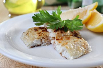 Dish of fish fillet with greens and lemon on table close up