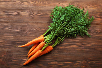 Fresh organic carrots with green tops on wooden background