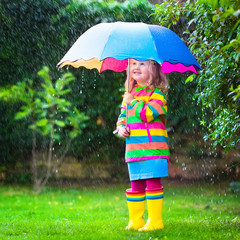 Little girl playing in the rain under colorful umbrella