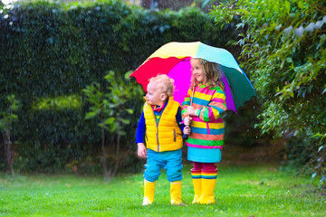 Kids playing in the rain under colorful umbrella