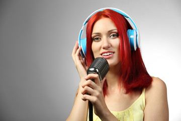 Beautiful young woman with microphone and headphones on gray background
