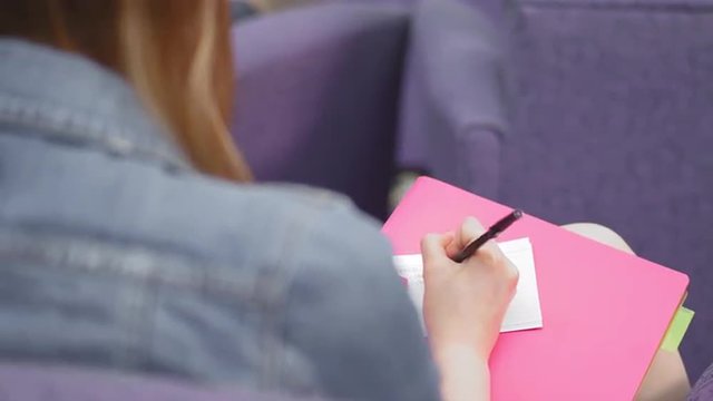 Close up of a student taking notes as her teacher conducts class
