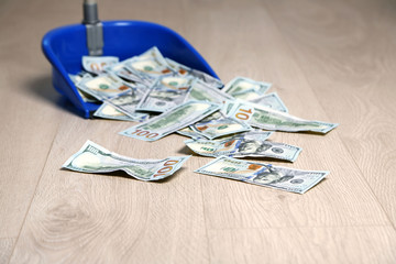 Dollars in garbage scoop on wooden floor background