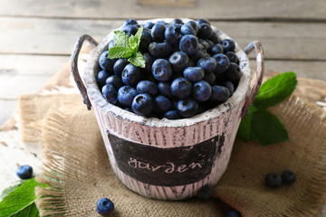 Tasty ripe blueberries with green leaves in bucket on table close up