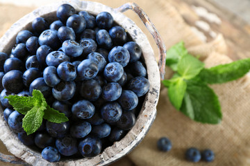 Tasty ripe blueberries with green leaves in bucket on table close up