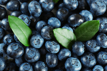 Tasty ripe blueberries with green leaves close up
