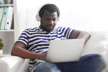 African American man listening music with headphones on sofa in room