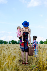 Female carrying valize with two children standing on wheat field