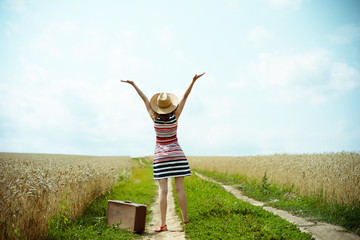 Backview of happy woman with old valize on countryside road