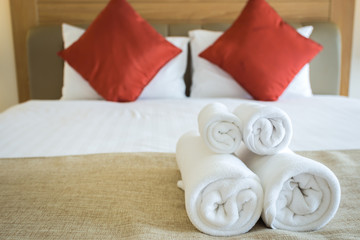 Close up of nice towels on white bed sheet with red pillow