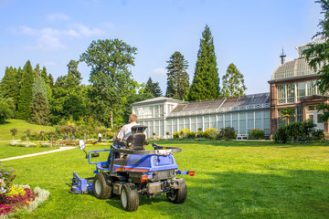 Mann mäht mit Aufsatzrasenmäher den Rasen in einem Landschaftspark 