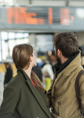 a couple looking at departure announcements in a train station