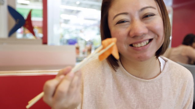 Happy Asian Woman eating sushi in a restaurant with smile face