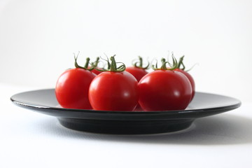 Circle of tomatos on simple black plate.