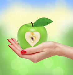 Big green apple in woman hand over blurred natural background