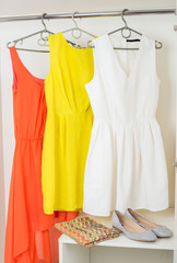 bright colorful dresses hanging on coat hanger, shoes and handba