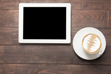 Digital tablet and coffee cup on wooden background