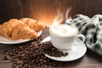 Breakfast coffee cup and croissant on wooden background
