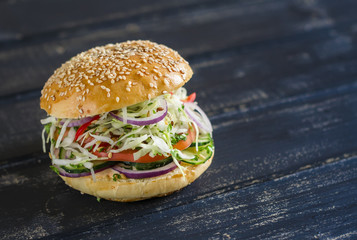 delicious veggie Burger - cabbage, tomato, cucumber, lettuce, and a homemade bun for burgers, on a dark wooden surface