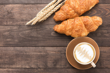 Coffee cup and fresh baked croissants on wooden background. Top