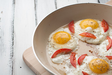 Hot pan with fried eggs and small pieces of tomato