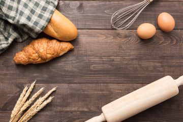 Freshly baked croissants, baguette and eggs on wooden background
