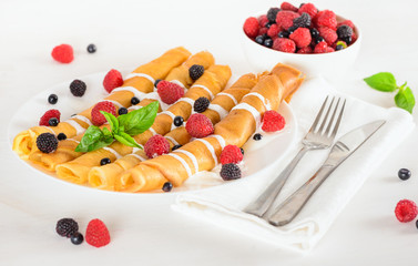  sweet crepes rolled in a tubes decorated cream and ripe berries
