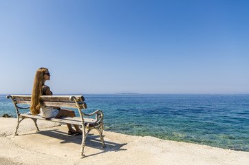 Young girl sitting on bench and looking at sea