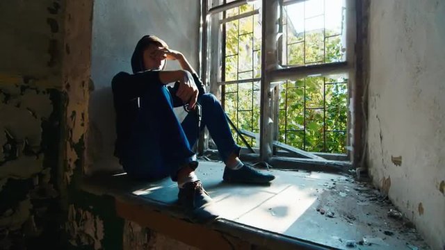 A man with a gun sitting on a window sill. Concept: despair