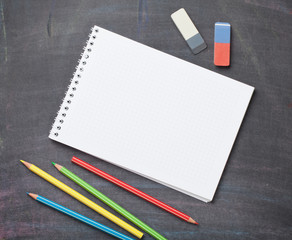 Blank notepad and colorful pencils on blackboard background