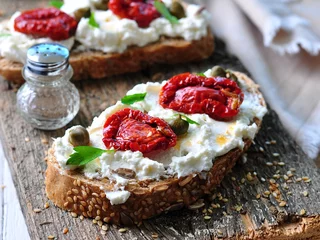  toast of rye bread with different seeds with ricotta cheese, sun-dried tomatoes, capers, parsley and olive oil. © chudo2307