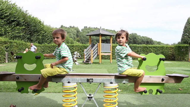 Two cute little boys, brothers, swinging in the park, happily, summertime