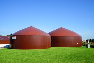 Grüne Wiese mit braunen  Gärbehältern einer Biogasanlage 