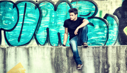 Attractive young man sitting against graffiti wall