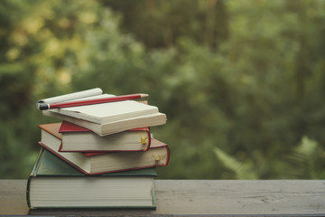 pile of books on a garden wooden table, green nature background