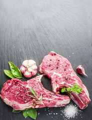 Raw beef steaks with spices on black cutting board.