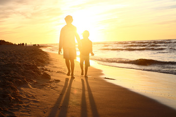 Spacer po plaży, zachód słońca. Dzieci chłopiec i dziewczynka spacerują brzegiem morza