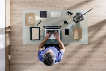 top view, a man sitting at tidy desk and working on his laptop