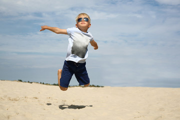 Umiem latać! Chłopiec podskakuje na piaszczystej plaży - obrazy, fototapety, plakaty