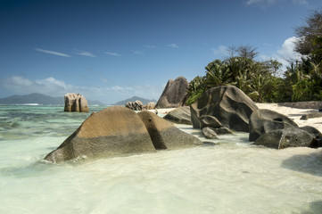 Naklejka premium View on untouched tropical beach Anse Source d'Argent with palm trees and bounders granite rocks, turquoise ocean and blue sky. Seychelles islands, La Digue.