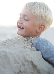 Zabawa na plaży.Wesoły chłopiec bawi się w piasku na plaży - obrazy, fototapety, plakaty